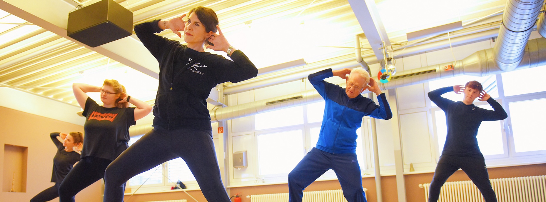 Foto: die Aktiv-Fitness-Trainerin zeigt Übungen und Teilnehmer von allen Altersklassen machen nach.