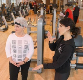 Seniorin in Sportkleidung wird im Fitnessstudio von der Trainerin beraten